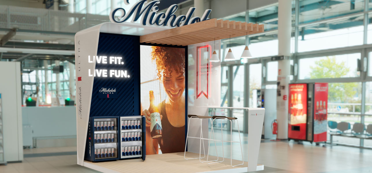 Visualización de un stand Michelob con el nombre elevado, cubierta de listones y panel gráfico central.